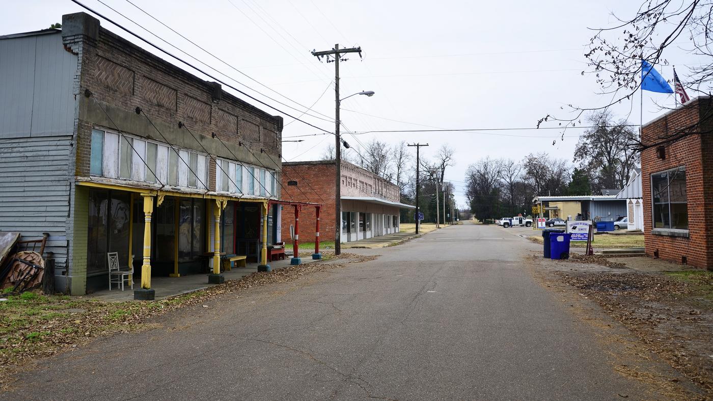 A row of boarded and shuttered brick storefronts on a quiet street in Friars Point, Mississippi